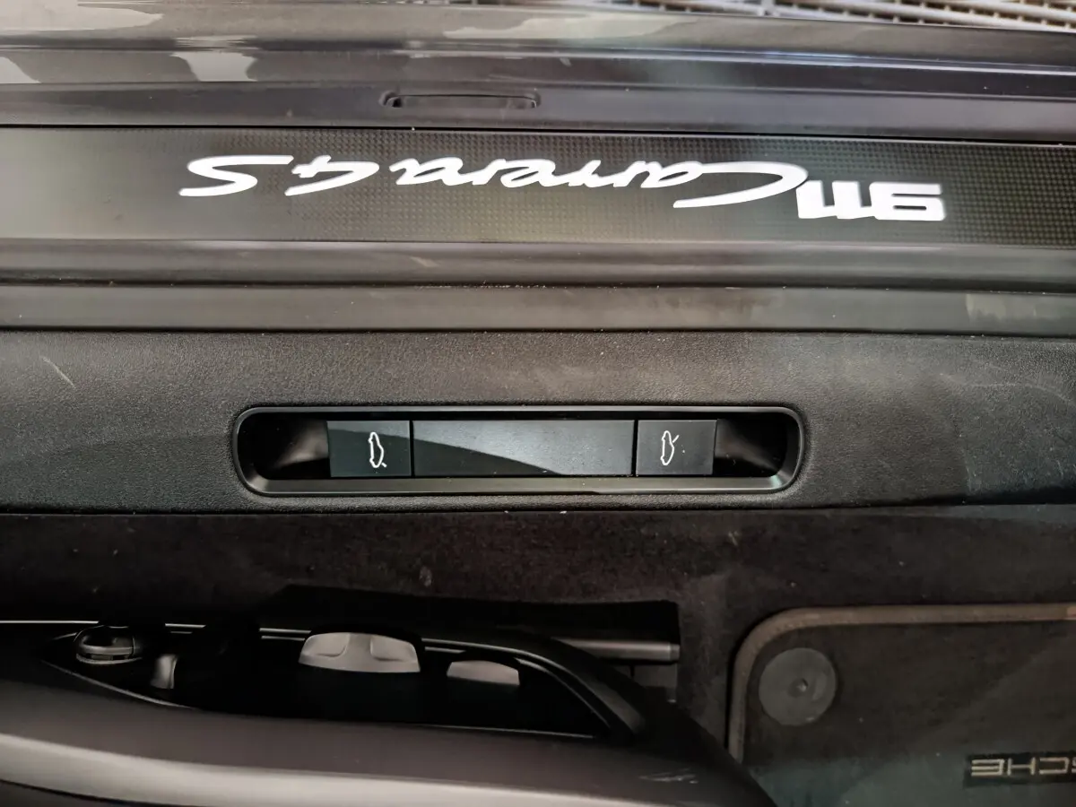 Gros plan sur la plaque de seuil de porte avec inscription Carrera 4S blanche sur fond gris foncé d'une Porsche 911.