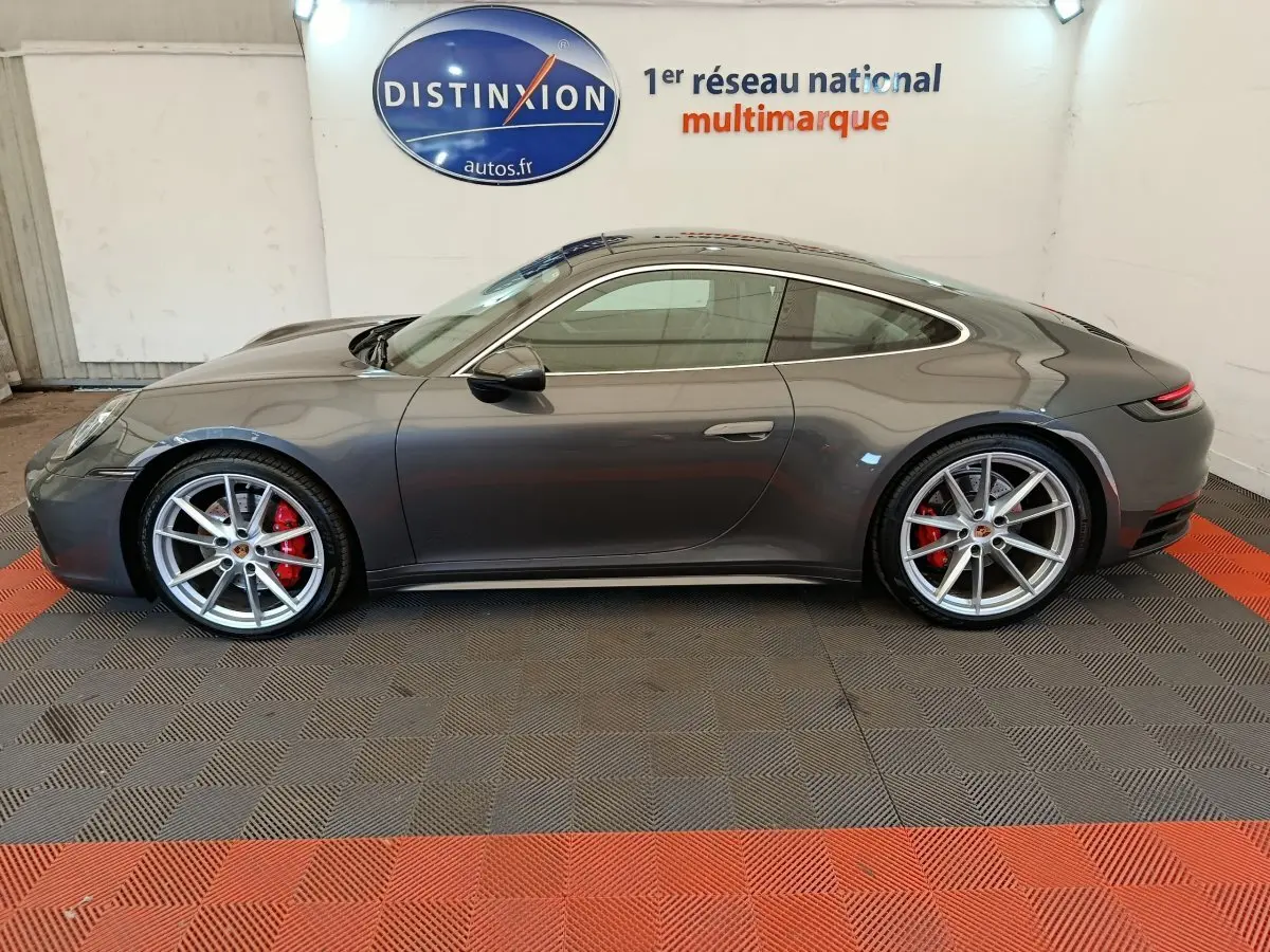 Profil droit d'une Porsche 911 Carrera 4S Coupé gris foncé avec jantes argentées et étriers de frein rouges, en intérieur showroom.