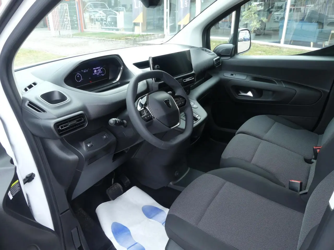 Intérieur côté conducteur du Peugeot Partner blanc 2025, avec tableau de bord moderne et sièges tissu gris.