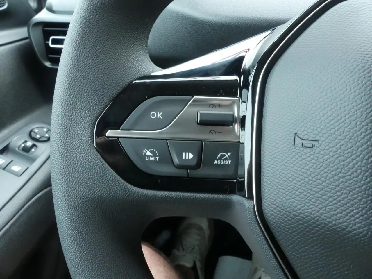 Gros plan sur les commandes gauche du volant noir du Peugeot Partner 2025, avec boutons multifonctions et levier de vitres.