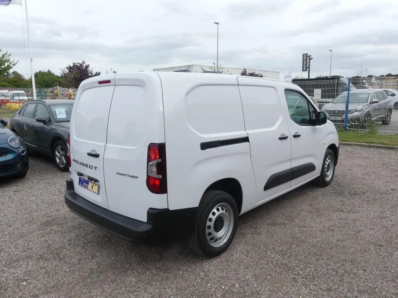 Vue 3/4 arrière droit d'un utilitaire Peugeot Partner blanc avec portes arrière battantes et protections latérales noires.