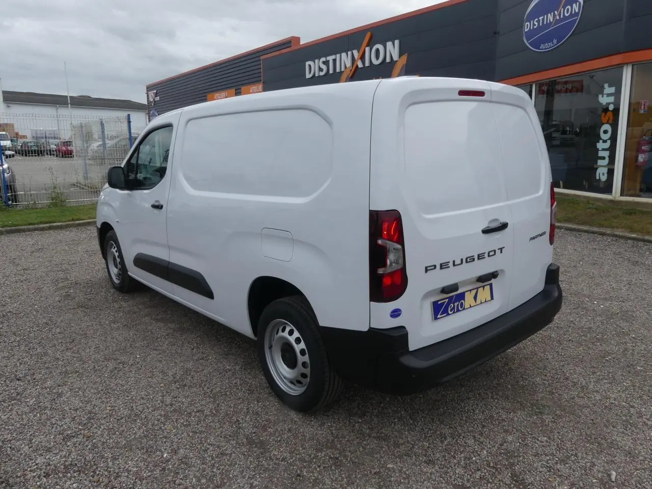 Vue 3/4 arrière droite d'un Peugeot Partner blanc avec portes arrière battantes et jantes tôle grises sur parking.