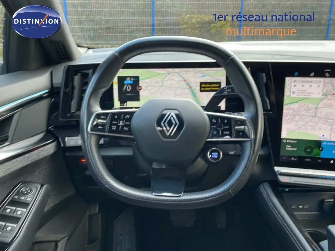 Vue intérieure centrée sur le volant Renault avec tableau de bord numérique et écran tactile affichant une carte.