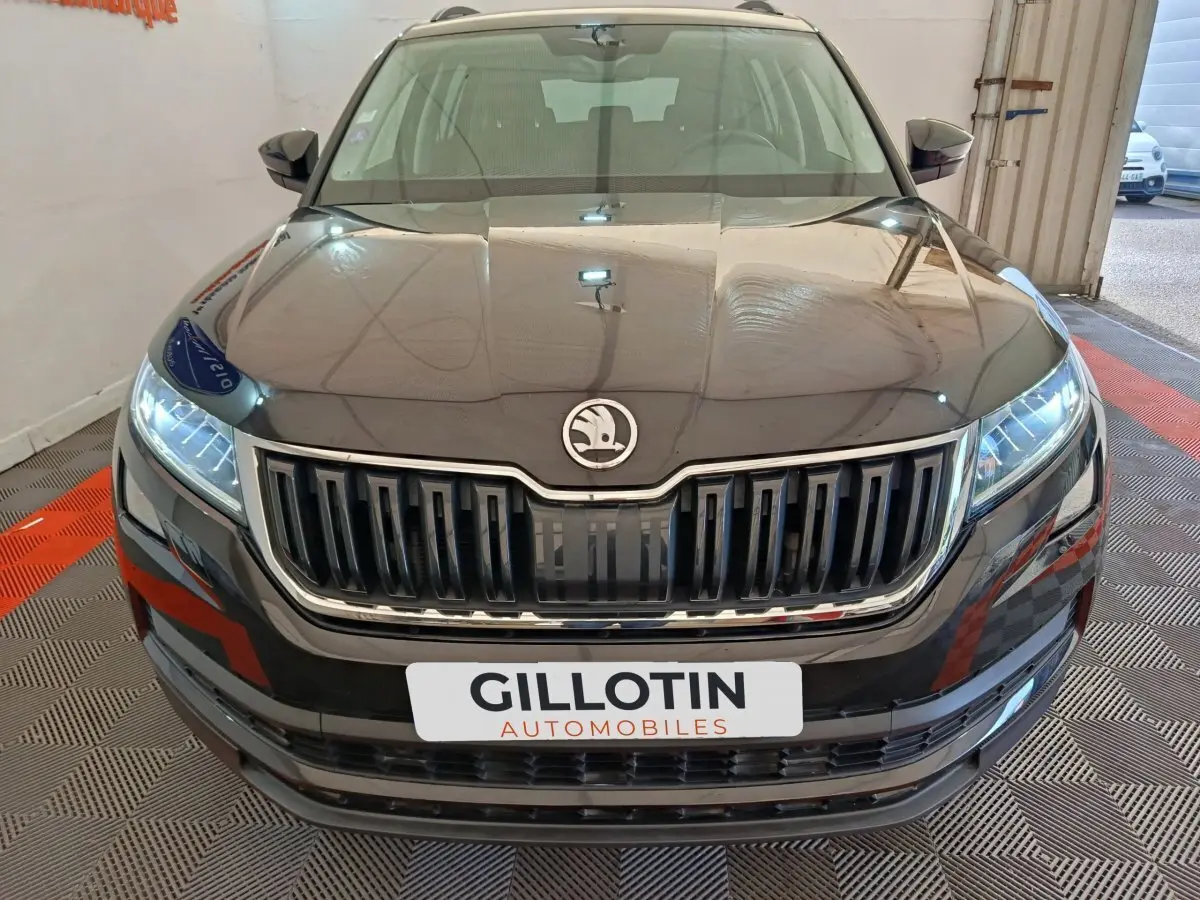 Vue frontale rapprochée d'un Skoda Kodiaq noir avec calandre verticale chromée et phares LED allumés.