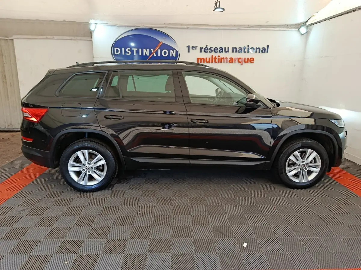 Profil côté droit d'un SUV SKODA KODIAQ noir 2021 garé en intérieur avec jantes alliage et barres de toit noires.