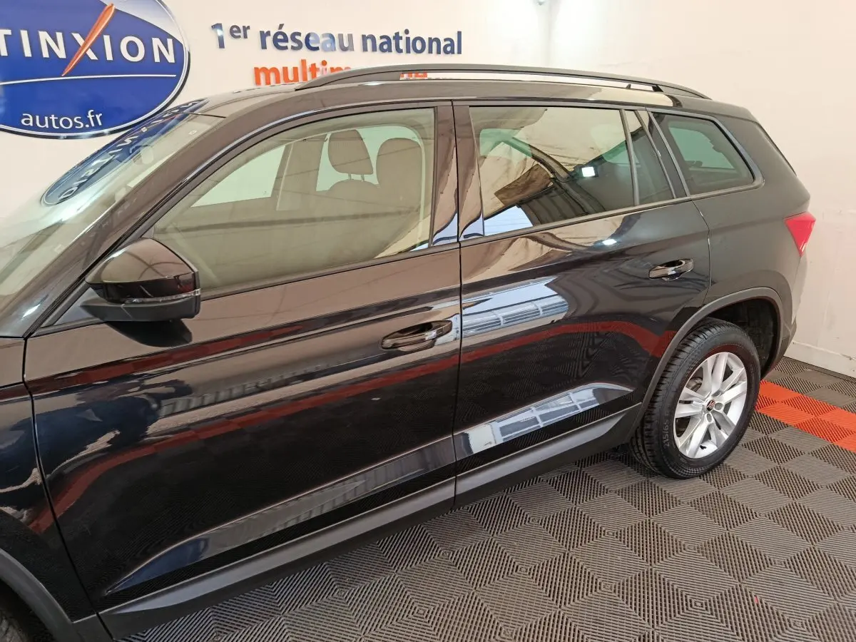 Vue latérale côté gauche d'un Skoda Kodiaq noir 2021 stationné en intérieur avec jantes alliage visibles.