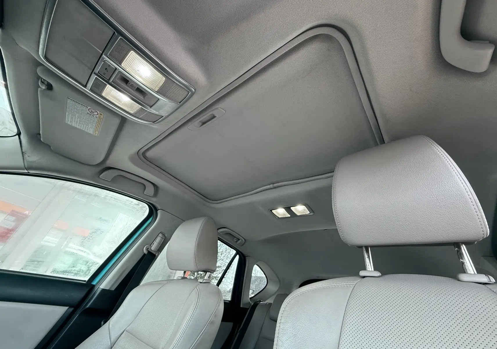 Vue intérieure du toit ouvrant et des sièges avant gris clair du Mazda CX-5 2013 bleu, avec éclairage intérieur allumé.