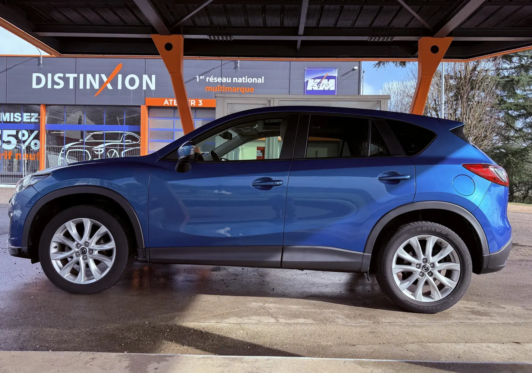 Vue latérale droite d'un Mazda CX-5 bleu 2013, soulignant ses jantes alliage et ses protections noires sur les bas de caisse.
