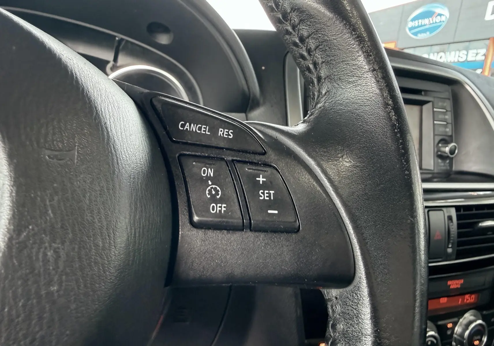 Gros plan sur les commandes de régulateur de vitesse au volant en cuir noir du Mazda CX-5 bleu de 2013.