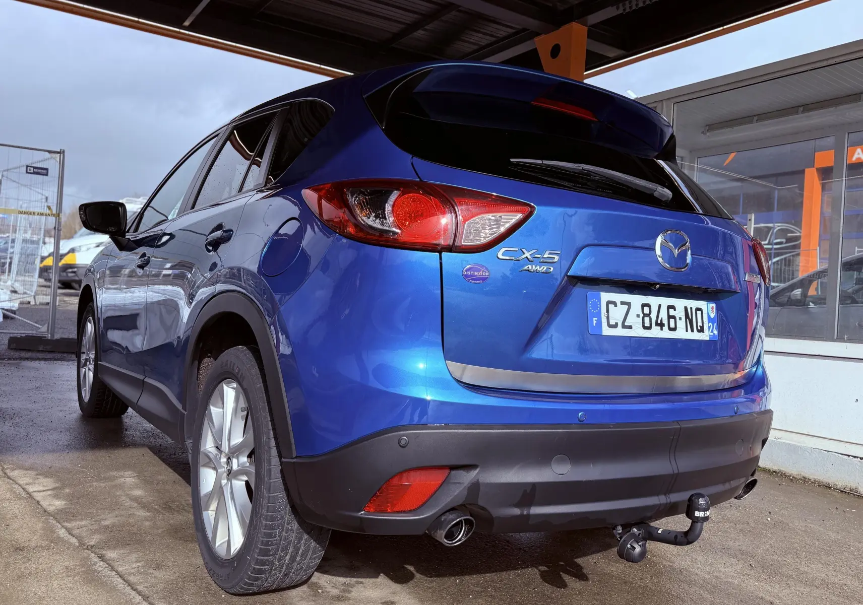 Vue 3/4 arrière droite d'un Mazda CX-5 bleu 2013 avec attelage et badges CX-5 AWD visibles.