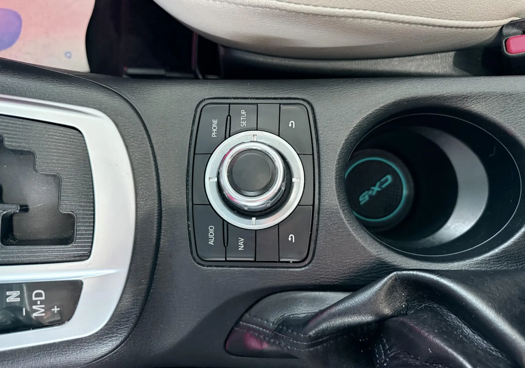 Gros plan sur la console centrale noire du Mazda CX-5 bleu 2013, avec molette de commande et porte-gobelet marqué CX-5.