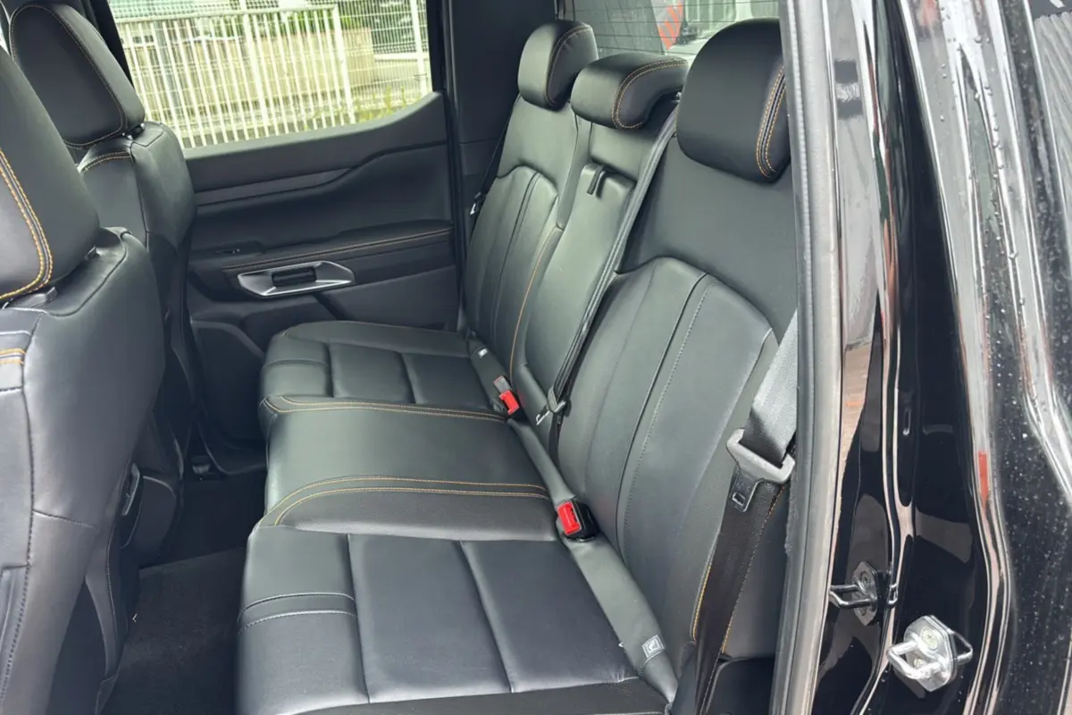 Vue latérale droite sur la banquette arrière en cuir noir avec surpiqûres orange du Ford Ranger Wildtrak 2025 noir agate.