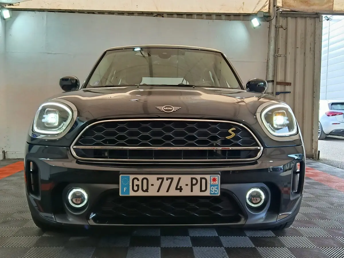 Vue frontale d'un MINI Countryman Cooper SE noir avec phares LED allumés et calandre hexagonale distinctive.