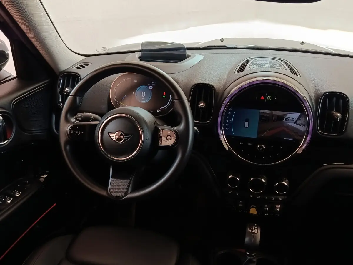 Vue intérieure du tableau de bord noir du MINI COUNTRYMAN Cooper SE avec volant multifonctions et écran tactile central rond.