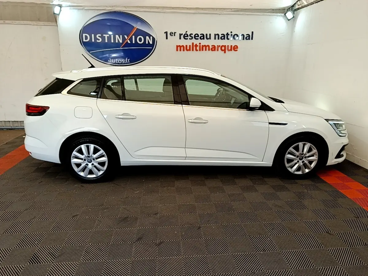 Profil droit d'une Renault Mégane Business E-Tech hybride rechargeable blanche, en intérieur avec logo Distinxion en arrière-plan.