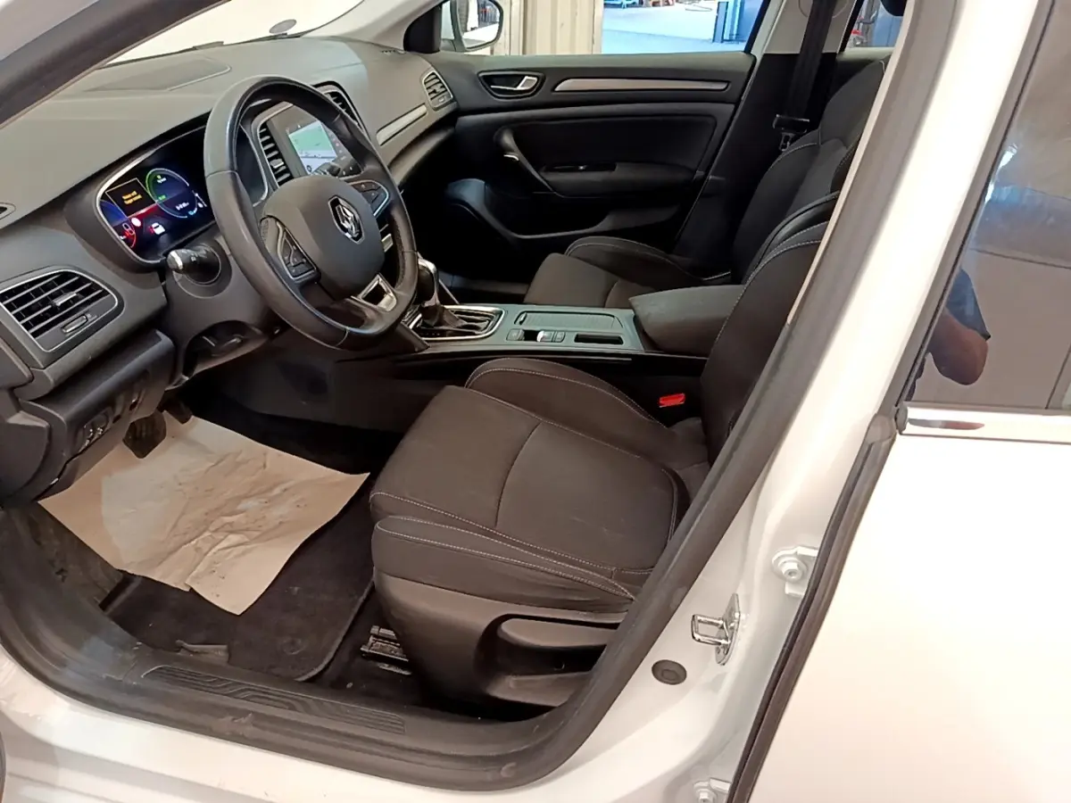 Vue intérieure côté conducteur d'une Renault Mégane Business E-Tech blanche, avec tableau de bord digital et sièges noirs.