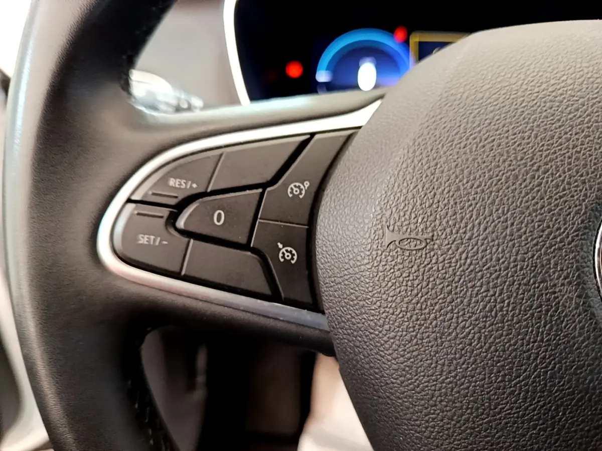 Gros plan sur les commandes du régulateur de vitesse au volant noir d’une Renault Mégane Business E-Tech hybride rechargeable blanche.