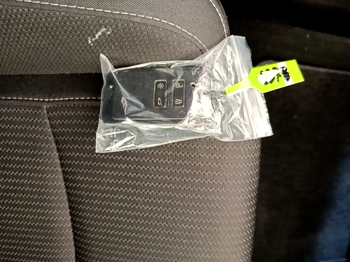 Télécommande Renault Megane Business E-Tech hybride blanche dans un sachet plastique posée sur un siège tissu gris foncé.