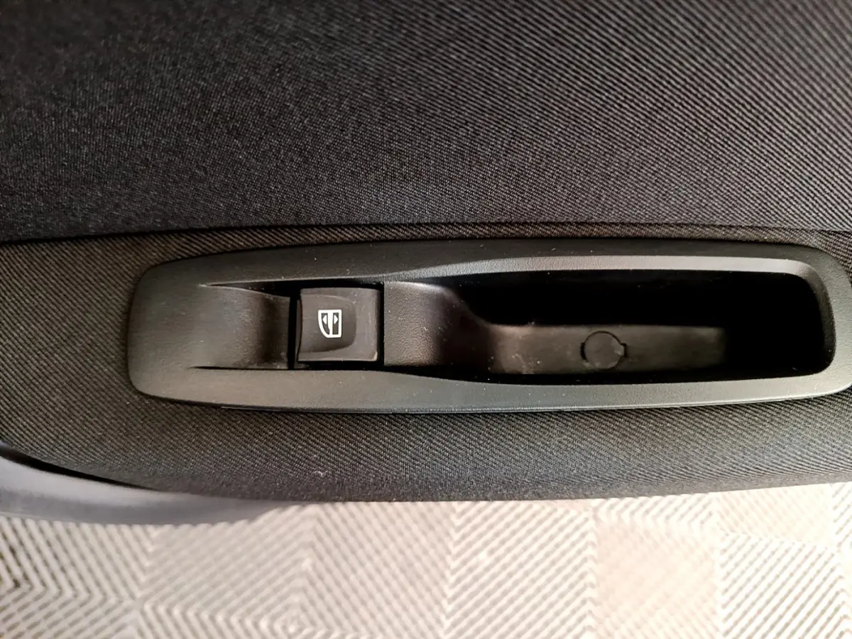 Gros plan sur le bouton de commande de la vitre électrique arrière dans la porte intérieure noire d’une Renault Megane blanche.