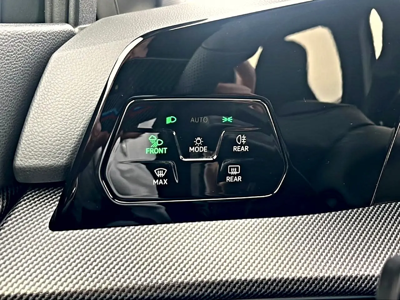Gros plan sur les commandes d’éclairage et de désembuage de la Volkswagen Golf 2026 avec finition noire brillante et insert carbone.