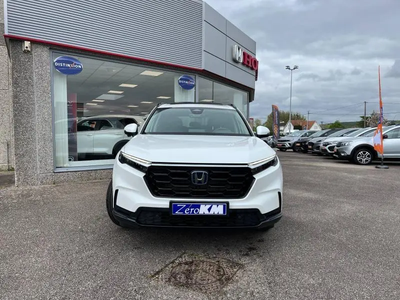 Vue frontale d'un Honda CR-V blanc platine nacrée 2024 avec calandre noire et plaque Zero KM visible.