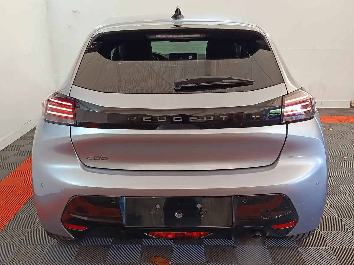 Vue arrière d'une Peugeot 208 gris clair 2025 avec feux LED allumés dans un garage.