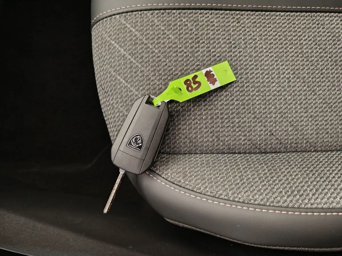 Clé Peugeot posée sur un siège tissu gris clair avec surpiqûres blanches, intérieur de Peugeot 208 2025.