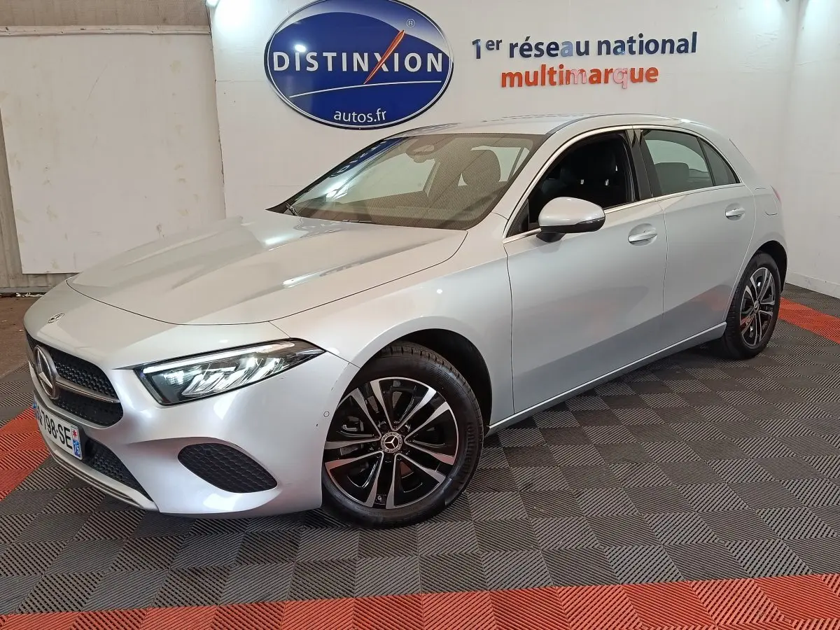Mercedes Classe A 250 e Business Line gris clair vue 3/4 avant droit en intérieur showroom avec jantes noires et chromées.