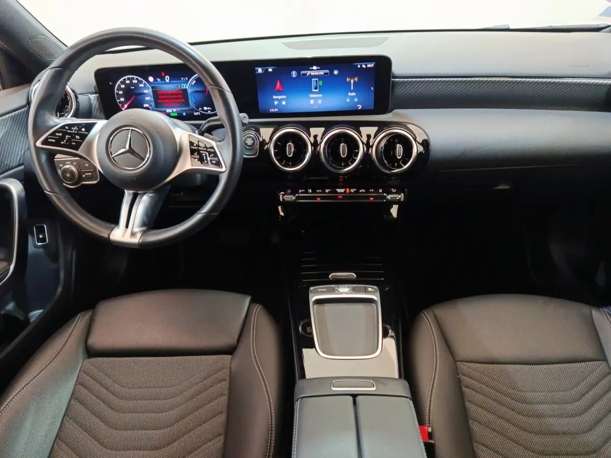 Vue intérieure avant de la Mercedes Classe A 250 e Business Line 2023, volant cuir alu et écran tactile central lumineux.