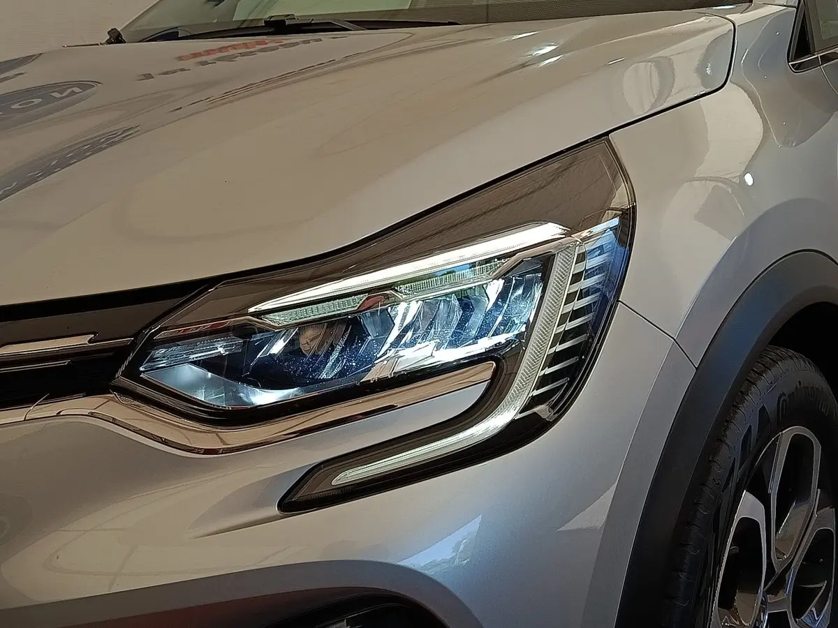 Gros plan sur le phare avant droit et la roue d’un Renault Captur gris clair Intens E-TECH Plug-in 2021.