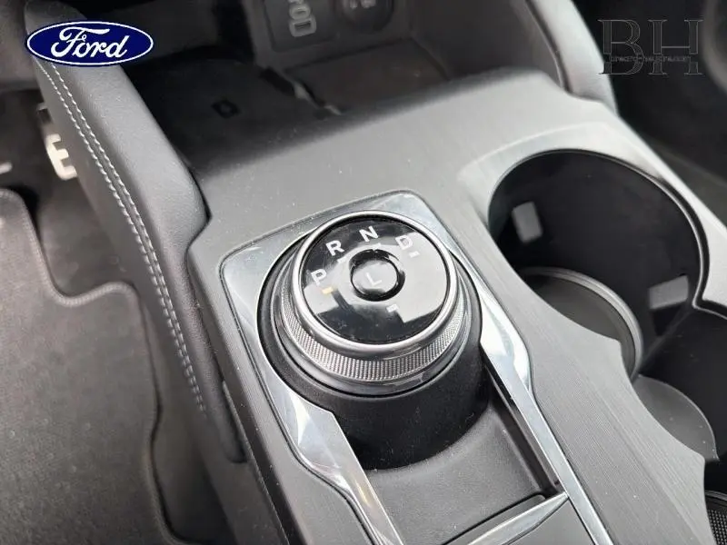 Gros plan sur la molette de sélection de la boîte automatique du Ford Kuga gris, avec console centrale et porte-gobelets visibles.