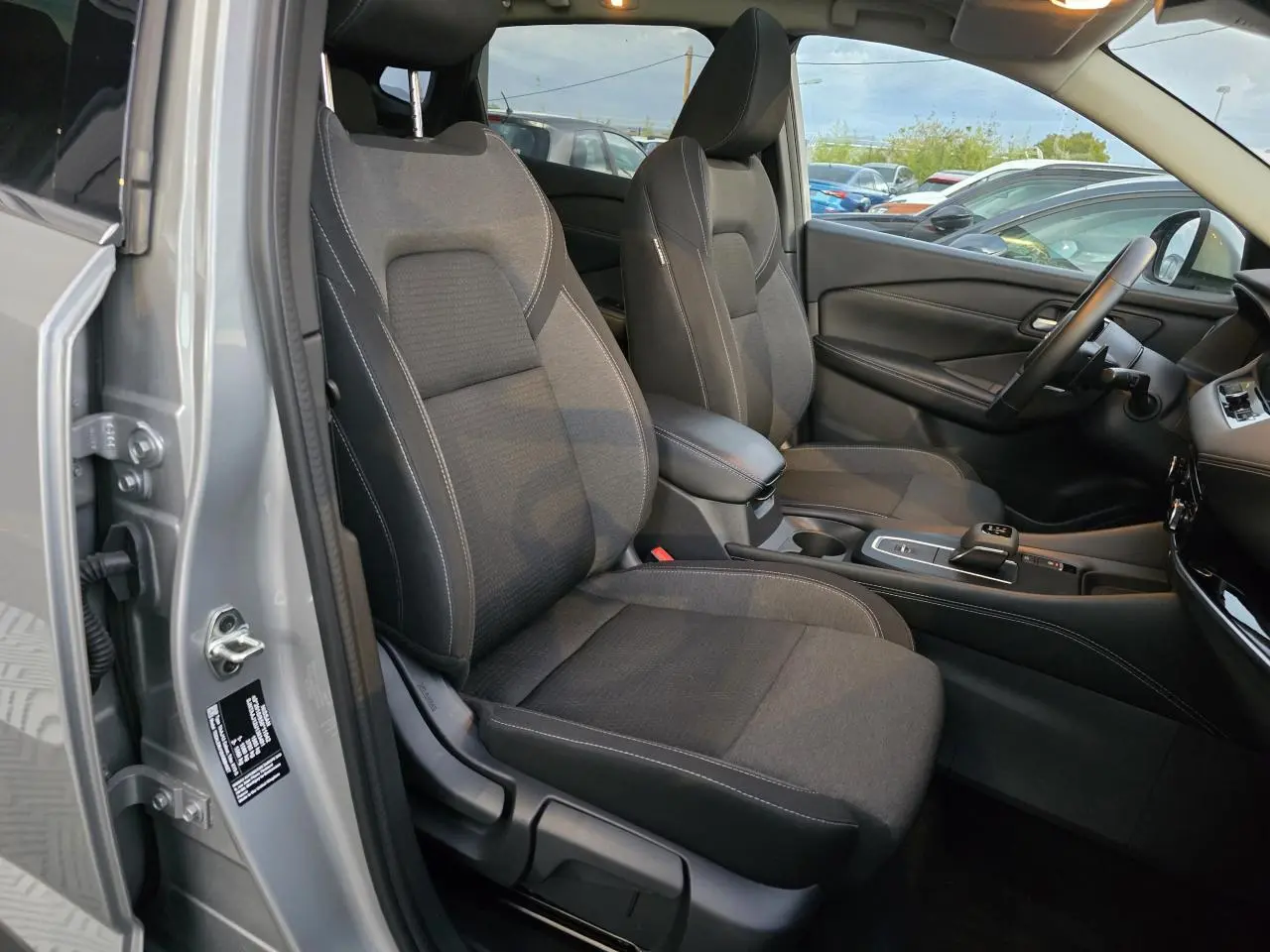 Vue intérieure côté conducteur du Nissan Qashqai gris silver 2024, mettant en valeur les sièges noirs et la console centrale moderne.