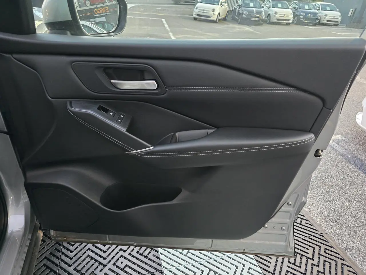 Porte intérieure côté gauche du Nissan Qashqai gris silver 2024, avec garniture noire et surpiqûres blanches visibles.