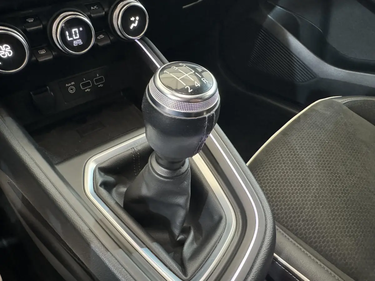 Gros plan sur le levier de vitesses manuel noir de la Renault Clio Intens 2020 avec console et siège tissu gris.