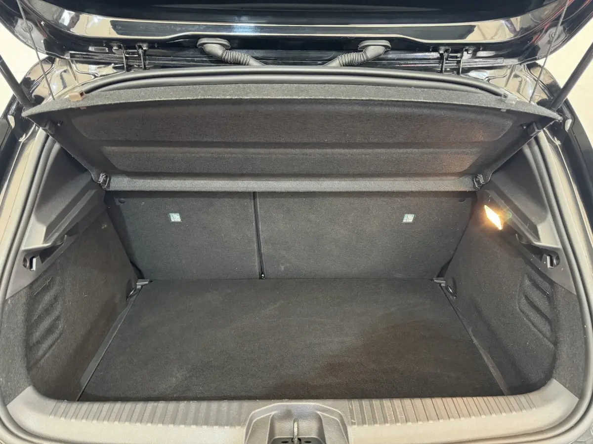 Coffre ouvert vu de l'arrière d'une Renault Clio Intens TCe 100 noire, montrant l'espace de chargement vide et la lumière intérieure.