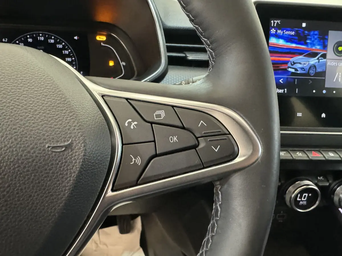 Gros plan sur les commandes droite du volant cuir de la Renault Clio Intens TCe 100 2020 avec écran tactile et tableau de bord partiel.