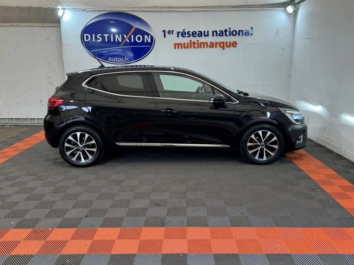 Profil côté gauche d'une Renault Clio Intens TCe 100 noire 2020, stationnée en intérieur sur sol à damiers gris et orange.
