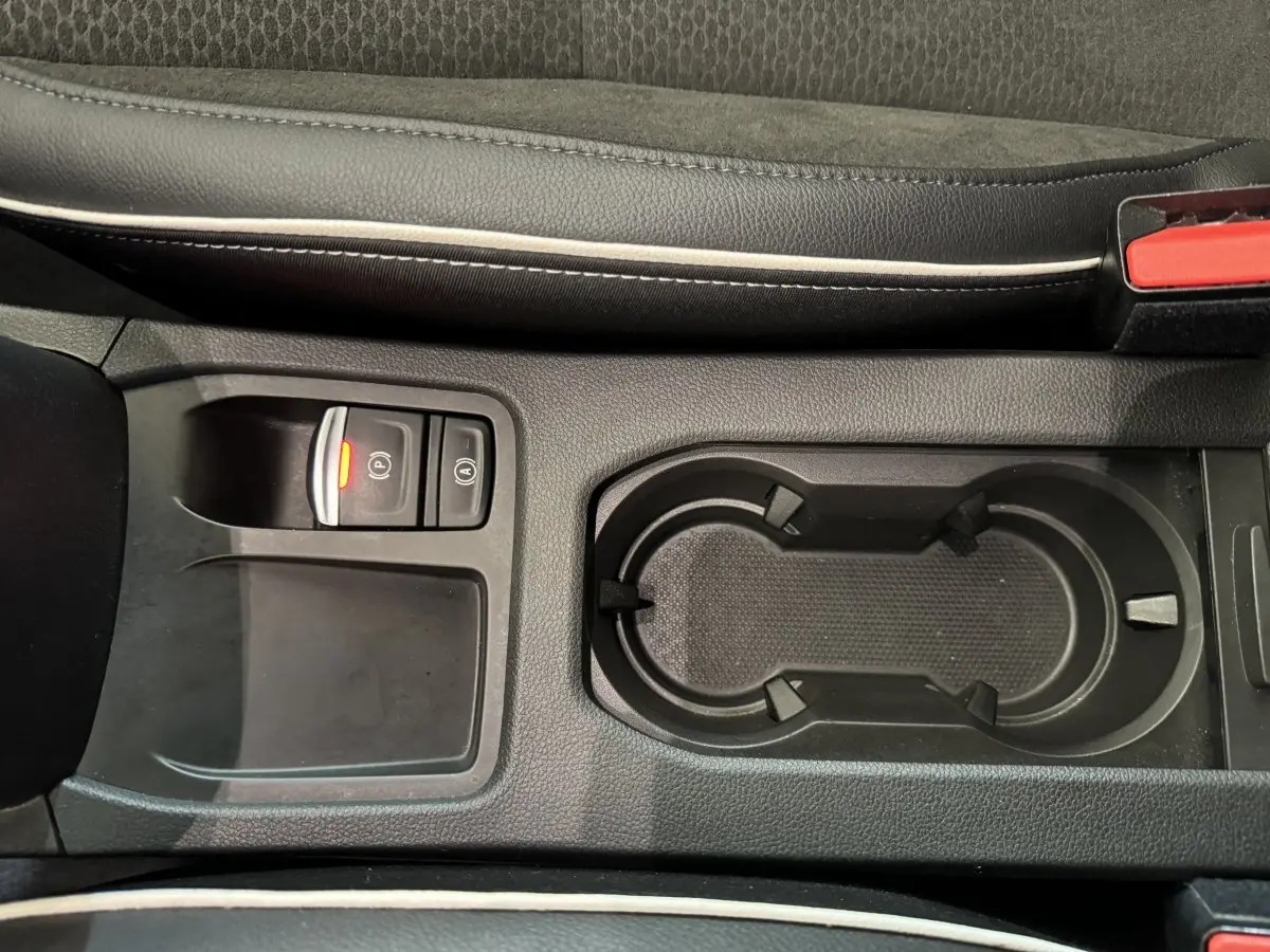 Gros plan sur la console centrale noire de la Renault Clio Intens TCe 100, avec frein à main électrique et porte-gobelets.