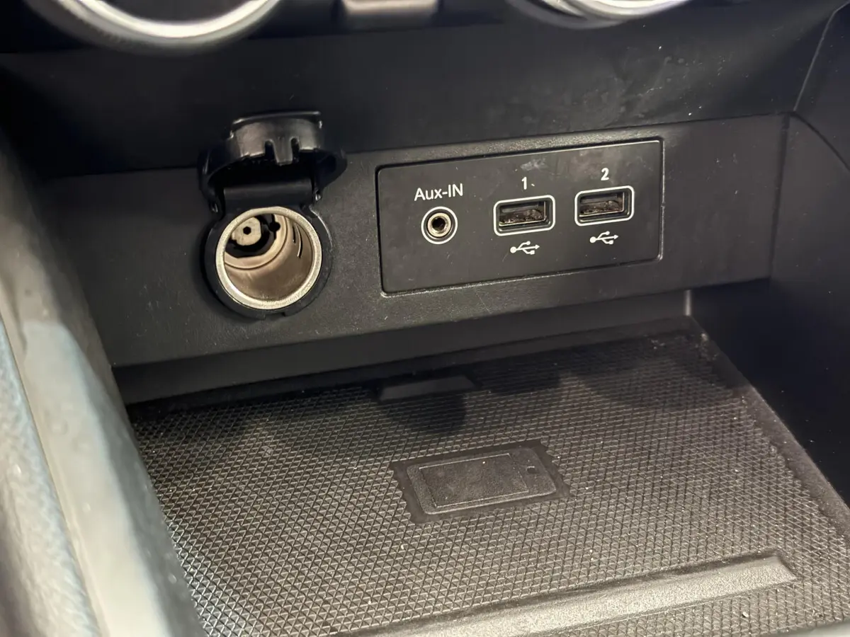 Vue rapprochée de la prise auxiliaire, deux ports USB et allume-cigare dans la console centrale d'une Renault Clio Intens noire 2020.