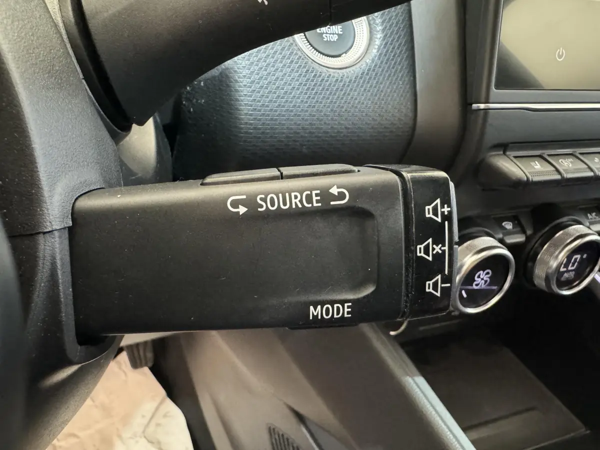 Gros plan sur la commande multimédia noire à gauche du volant dans l'habitacle de la Renault Clio Intens 2020.