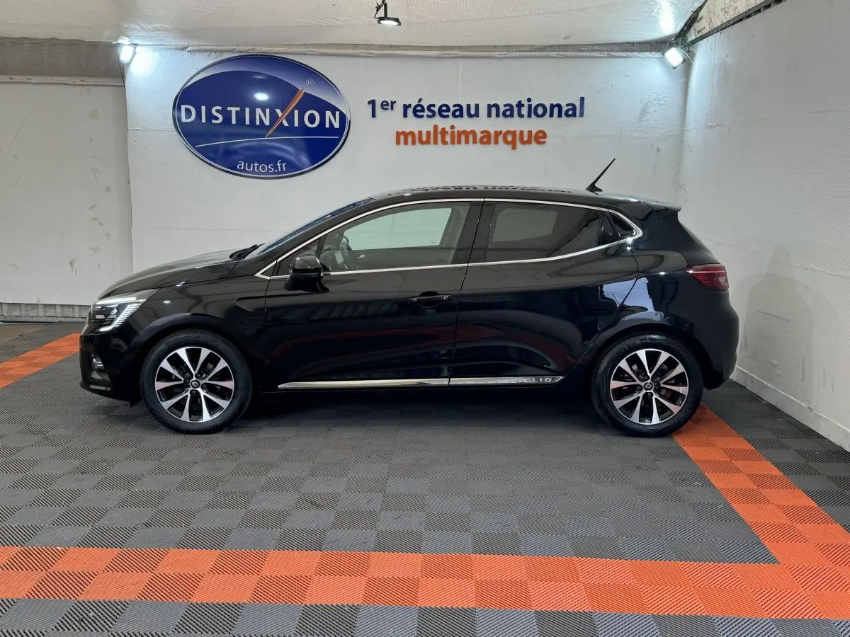 Profil côté gauche d'une Renault Clio Intens noire 2020 avec jantes alliage et vitres teintées en intérieur showroom.