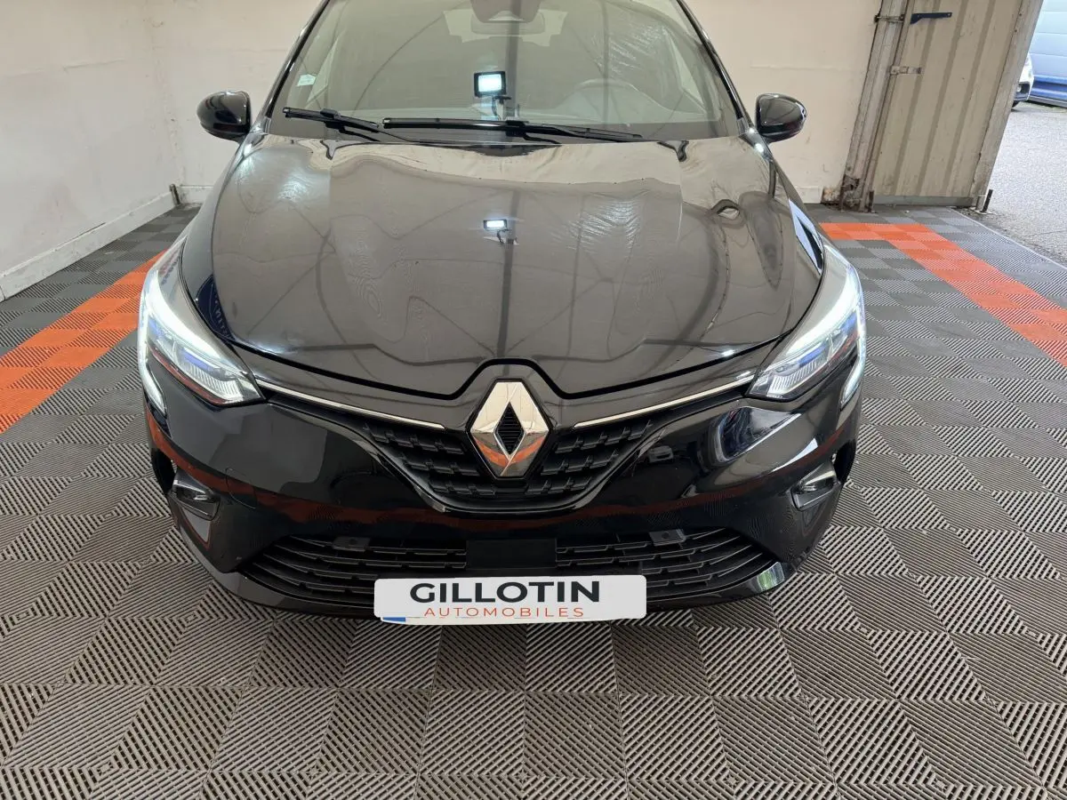 Vue frontale rapprochée d'une Renault Clio Intens TCe 100 noire avec phares LED allumés en intérieur.