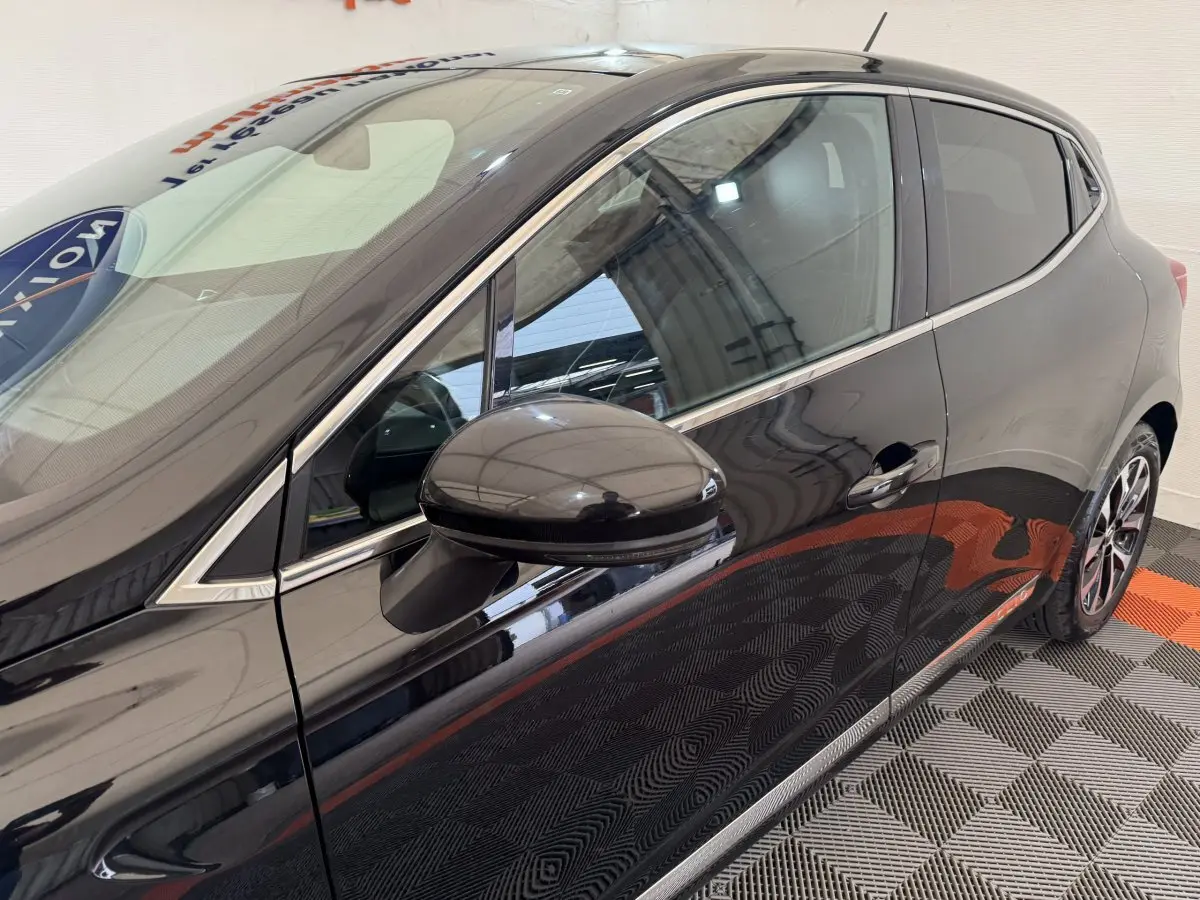 Vue latérale côté gauche d'une Renault Clio Intens TCe 100 noire, mettant en valeur la poignée et le rétroviseur extérieur.