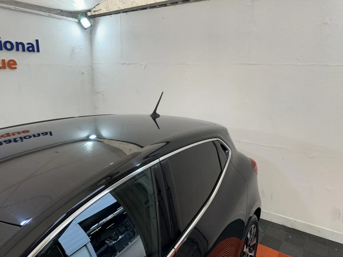 Vue arrière côté gauche d'une Renault Clio Intens TCe 100 noire, avec vitres teintées et antenne de toit.