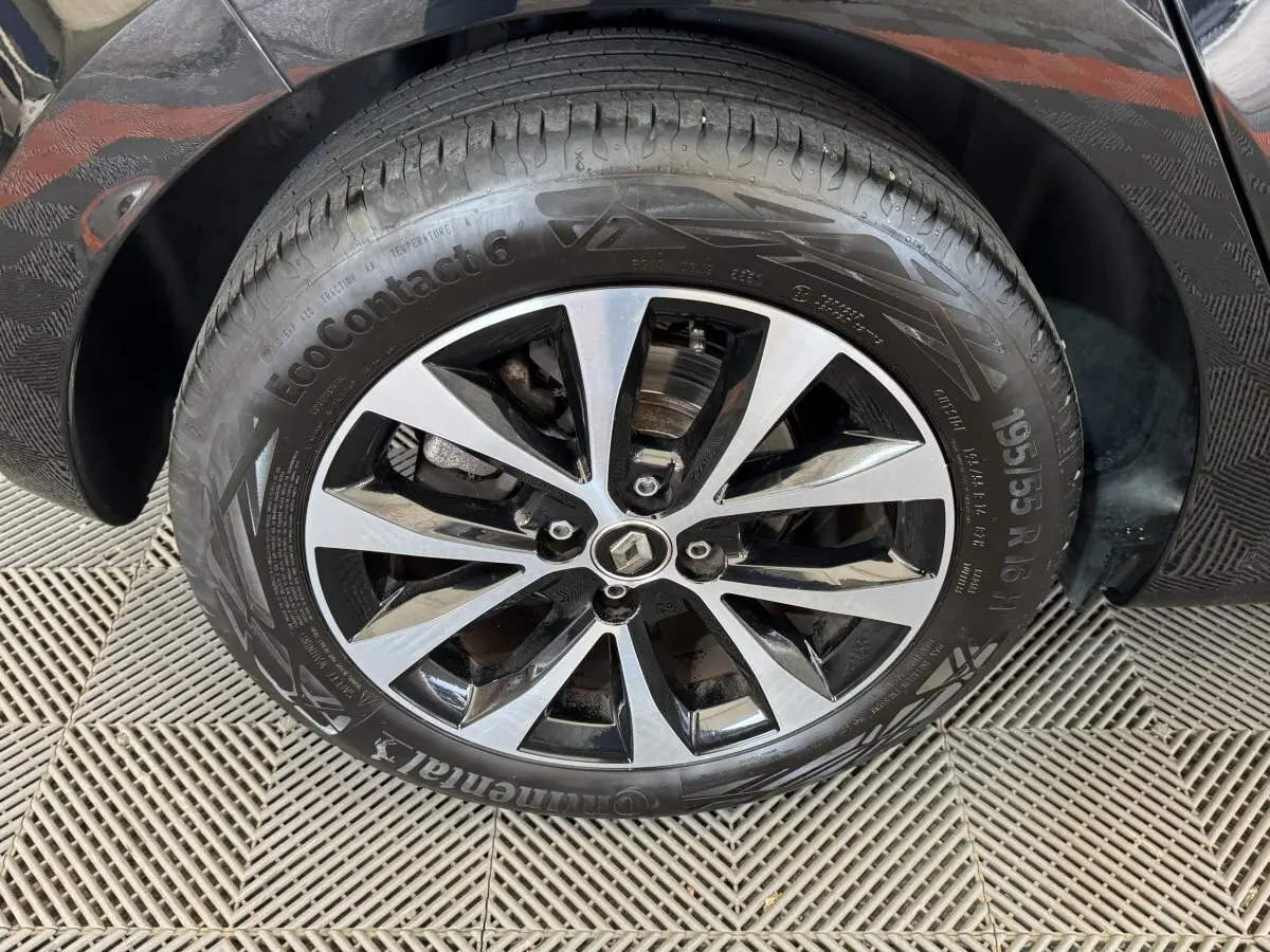 Gros plan sur la roue avant gauche noire d'une Renault Clio Intens TCe 100 avec jante alliage bicolore.