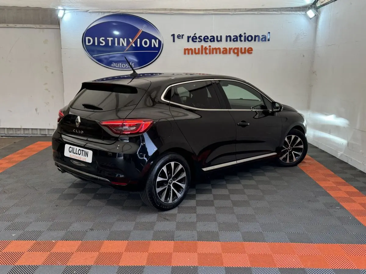 Renault Clio Intens TCe 100 noire vue en 3/4 arrière droit dans un showroom avec sol gris et bandes orange.