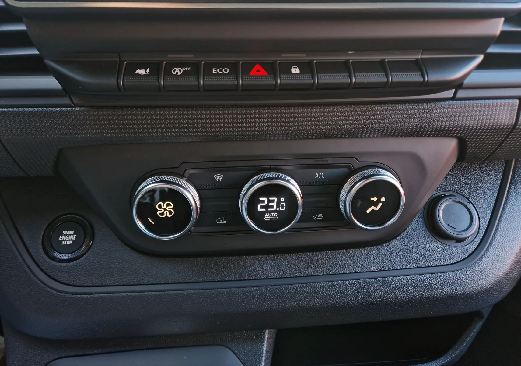 Gros plan sur la console centrale noire du Renault Trafic Fourgon 2025, montrant les commandes de climatisation et le bouton start/stop.