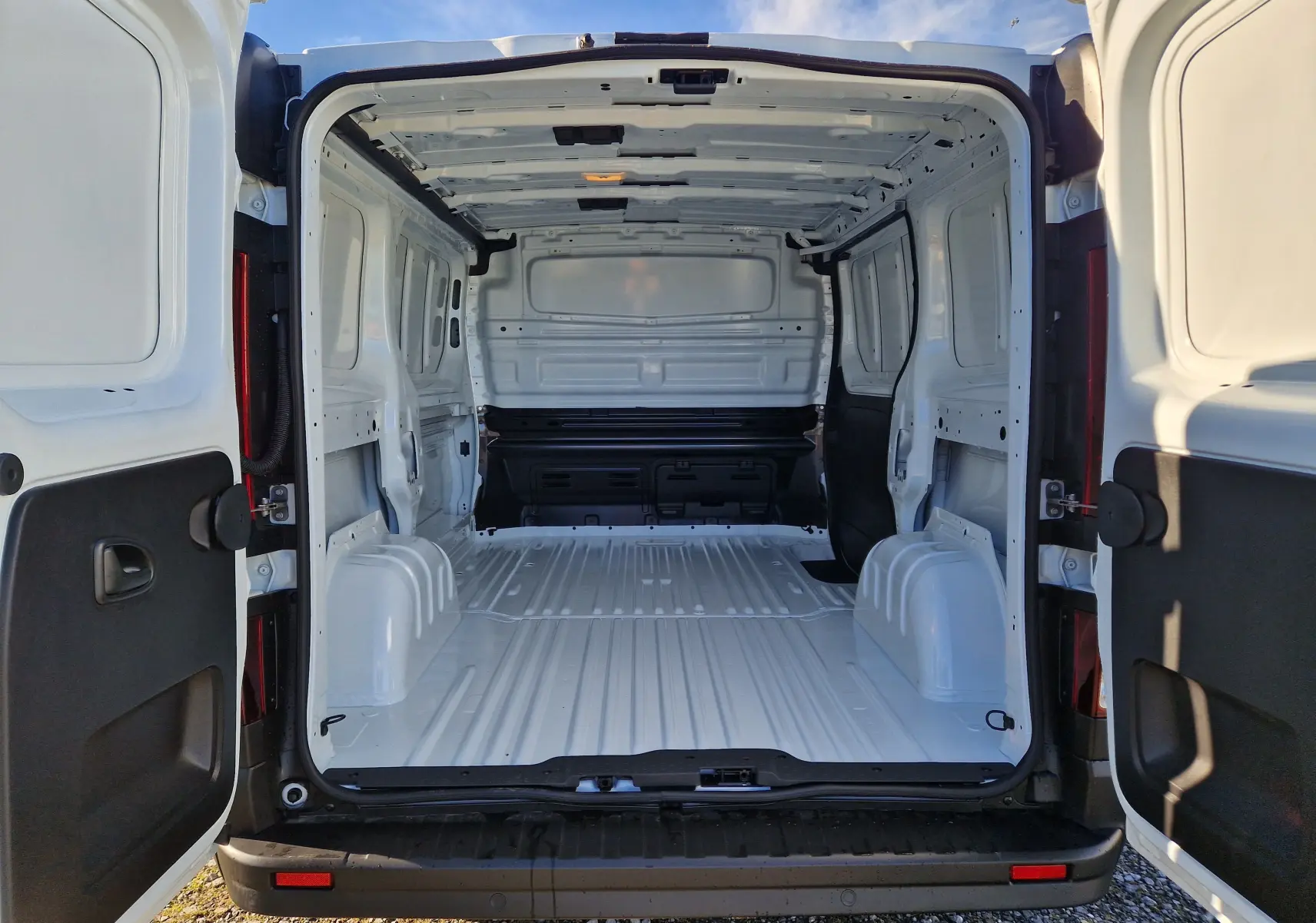 Vue arrière ouverte du Renault Trafic Fourgon blanc 2025, montrant l’espace de chargement vide et la structure intérieure métallique.