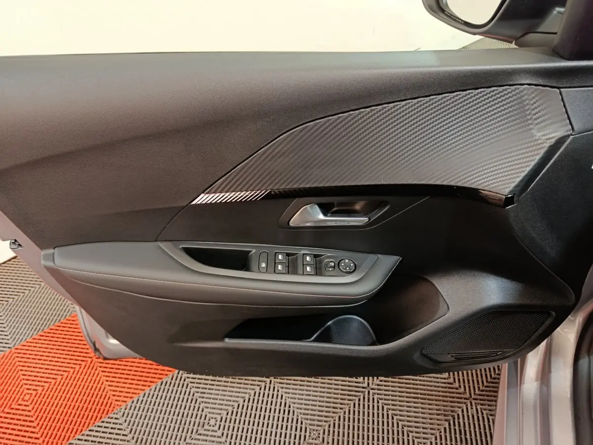 Vue intérieure de la porte avant gauche gris clair de la Peugeot 208 PureTech 100 S&S Allure avec commandes électriques et insert carbone.