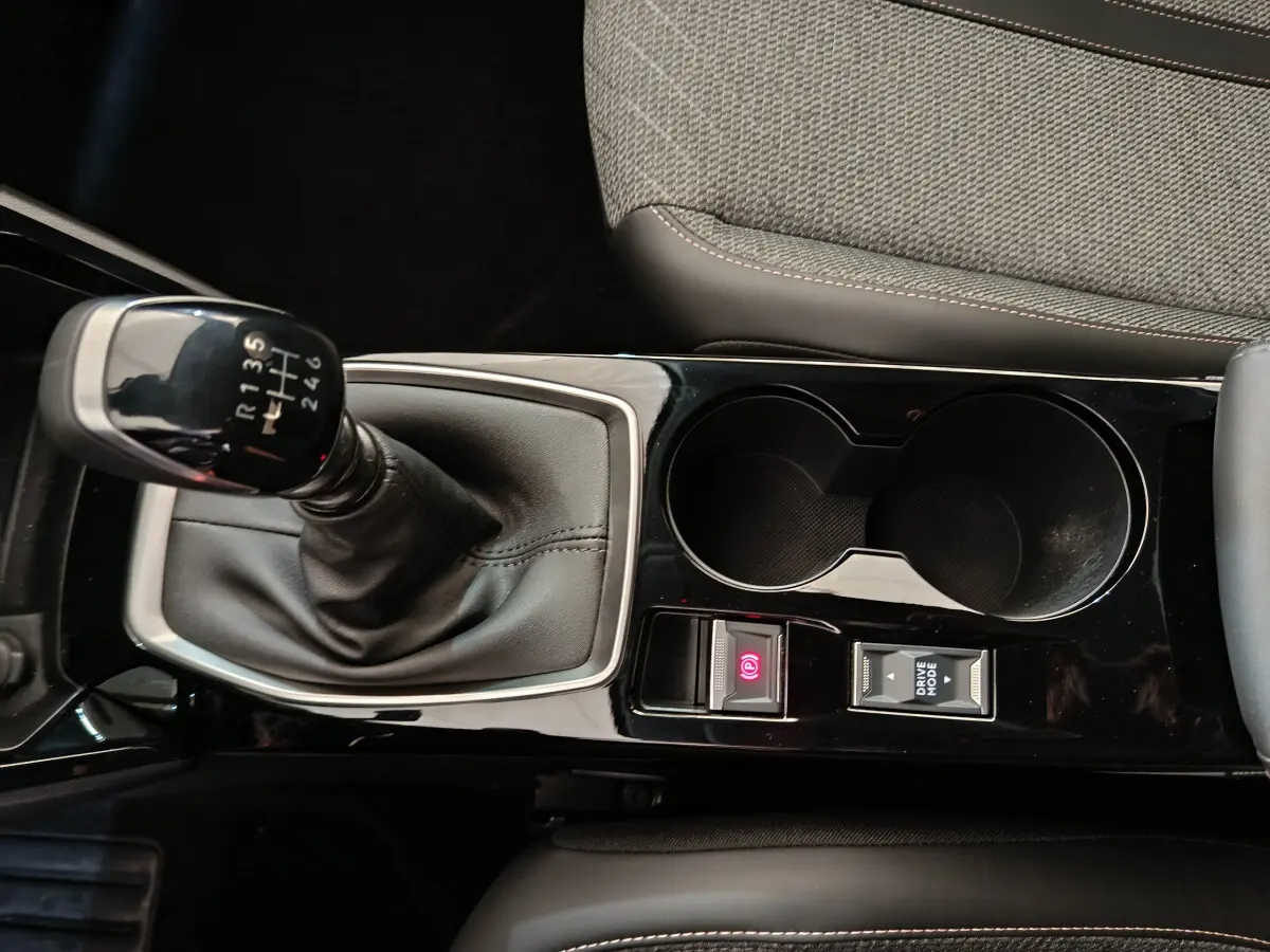 Gros plan sur la console centrale noire brillante de la Peugeot 208 PureTech 100 avec levier de vitesse manuel et boutons électroniques.